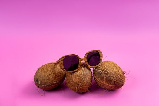 three whole coconuts and wooden glasses on a pink background.