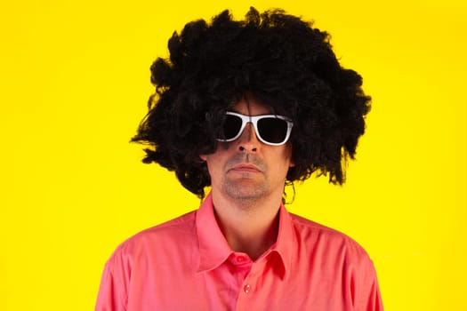 Curly man wearing sunglasses looking at camera on yellow background