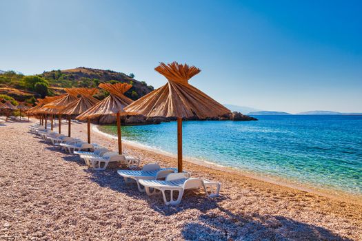 Girl relaxing on the deck chair while reading a book under a straw umbrella in the Oprna beach, Krk island, Croatia