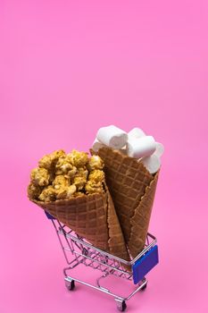 Shopping cart with ice cream cones with sweets on a pink background.