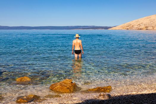 Young man with straw hat in the sea water on beach during the summer vacation, Stara Baska. krk. Croatia