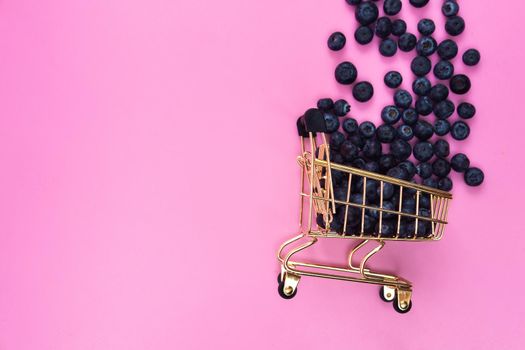Blueberries in a grocery cart on a pink background. Scattered blueberries near a grocery cart on a pink background
