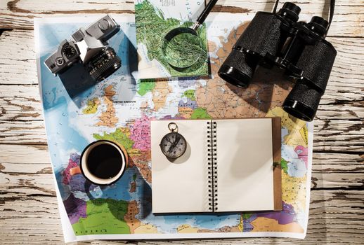 Flat lay of the travel planning concept. Top view of a diary, binoculars, compass, retro photo camera, coffee, and Europe map on a white wooden table