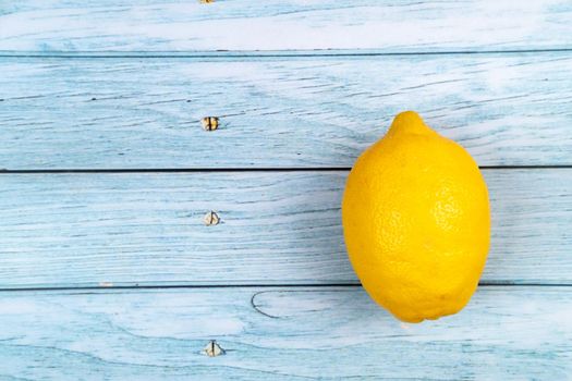 A whole yellow lemon lies on a blue wooden background.