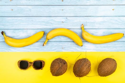 bananas, coconuts and sunglasses in lies on a blue wooden background and a yellow background.