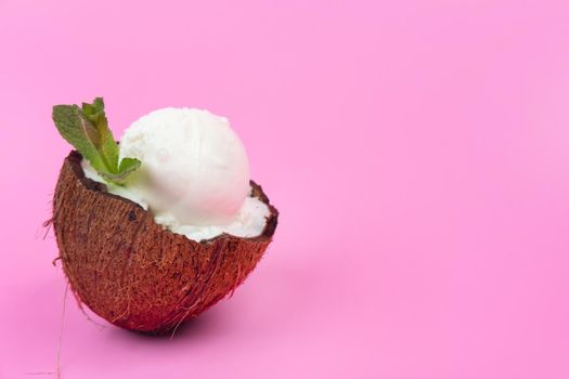 Vanilla ice cream balls in fresh coconut halves, decorated with mint leaves on a pink background.