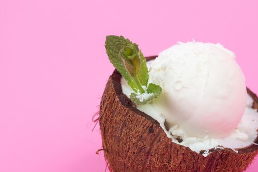 Vanilla ice cream balls in fresh coconut halves, decorated with mint leaves on a pink background.