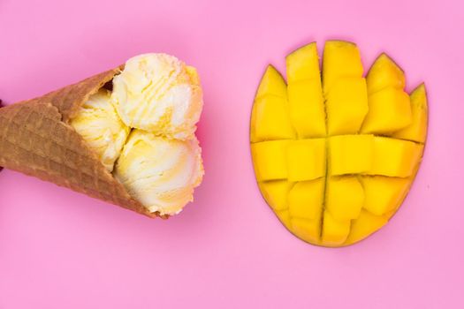 Mango-flavored ice cream balls in a waffle cone on a pink background. Ripe mango with ice cream on a pink background