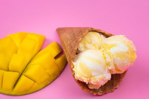 Mango-flavored ice cream balls in a waffle cone on a pink background. Ripe mango with ice cream on a pink background