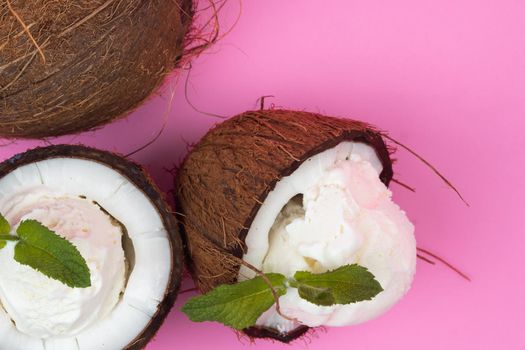 Vanilla ice cream balls in fresh coconut halves decorated with mint leaves on a pink background.