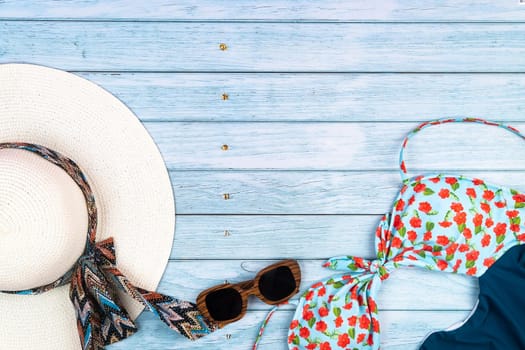 Top view of a straw white hat with glasses and a swimsuit, lying on a blue wooden background.Summer vacation concept.