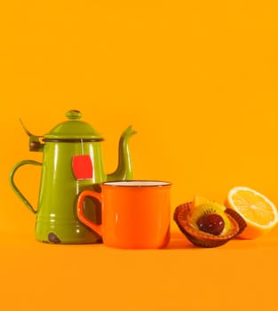 Set of vintage teacup, orange cup, lemon and pastry on orange background. Copy space on top