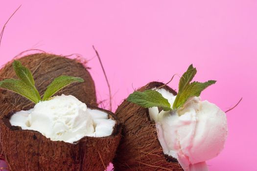 Vanilla ice cream balls in fresh coconut halves decorated with mint leaves on a pink background.