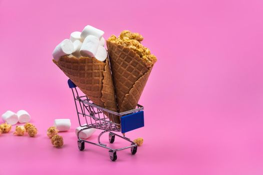 Shopping cart with ice cream cones with sweets on a pink background.