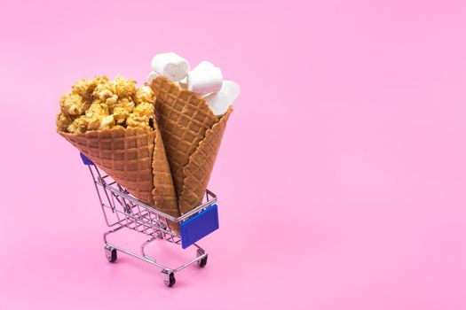 Shopping cart with ice cream cones with sweets on a pink background.