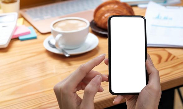 Mockup image blank white screen cell phone.women hand holding texting using mobile on desk at home office..