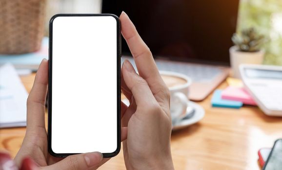 Mockup image blank white screen cell phone.women hand holding texting using mobile on desk at home office..