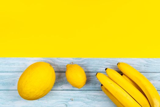 An assortment of yellow fruits lies on a blue wooden background and a yellow background.