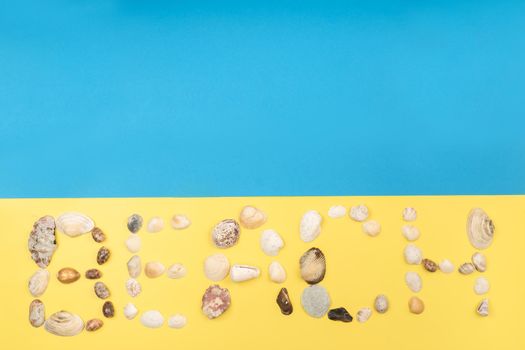 The inscription of the word beach is made of shells on a yellow-blue background.Travel concept.