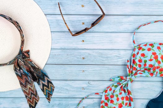 Top view of a straw white hat with glasses and a swimsuit, lying on a blue wooden background.Summer vacation concept.