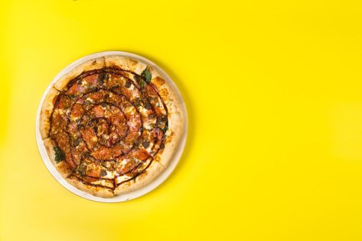 Delicious large pizza with bacon and spinach on a yellow background.