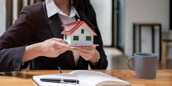 Hands of young woman holding model house..