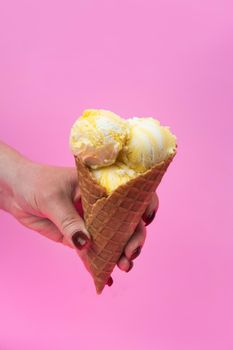 A hand holds an ice cream cone on a pink popsicle background in a waffle cup