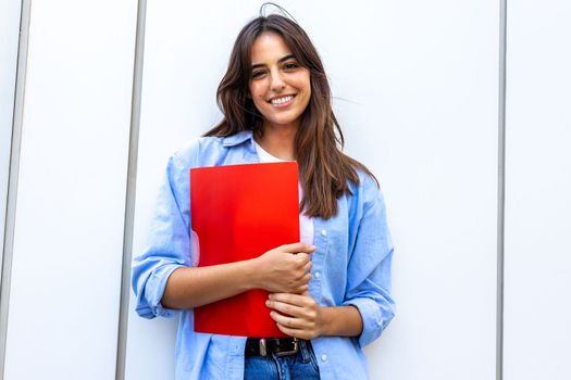 Happy, smiling female college student looking at camera holding red folder. Education concept.