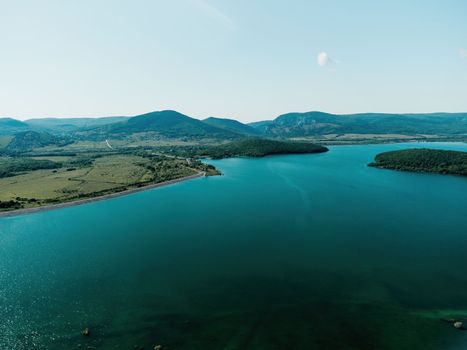 Aerial landscape from flying drone storage reservoir at mountain foot covered colorful spring forest. Beautiful view from above blue lake among highlands