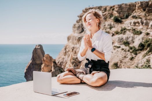 Happy girl doing yoga with laptop working at the beach. beautiful and calm business woman sitting with a laptop in a summer cafe in the lotus position meditating and relaxing. freelance girl remote work beach paradise