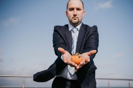 Male persimmon park. Hipster millennial man in a tie and jacket bites off a persimmon while sitting on a park bench in slow motion Young business people eat golden persimmons at lunchtime