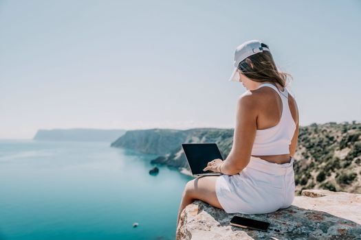 Digital nomad, Business woman working on laptop by the sea. Pretty lady typing on computer by the sea at sunset, makes a business transaction online from a distance. Freelance remote work on vacation