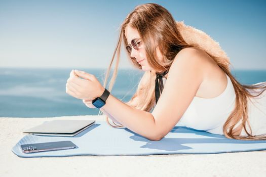 Successful business woman in yellow hat working on laptop by the sea. Pretty lady typing on computer at summer day outdoors. Freelance, travel and holidays concept.