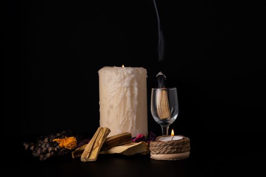 palo santo ,holy stick smoking in a glass cup with lighted candles and white background