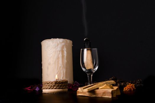 palo santo ,holy stick smoking in a glass cup with lighted candles and white background