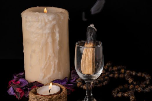 palo santo ,holy stick smoking in a glass cup with lighted candles and white background