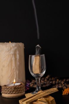 palo santo ,holy stick smoking in a glass cup with lighted candles and white background