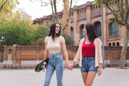 two young women friends walking happy holding hands through the city, concept of female friendship and love