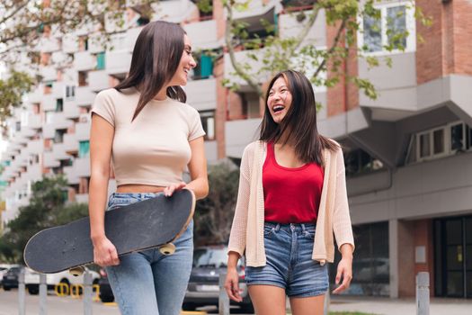 two young women friends laughing and walking happy through the city, concept of female friendship and teenager lifestyle