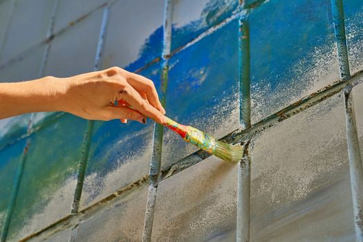 an implement with a handle, consisting of bristles, hair, or wire set into a block, used for cleaning, applying a liquid or powder to a surface. Female hand painting a wall with a brush in blue.
