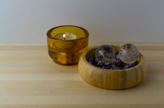 Crystal balls with amethyst stones and a burning candle on a wooden table.