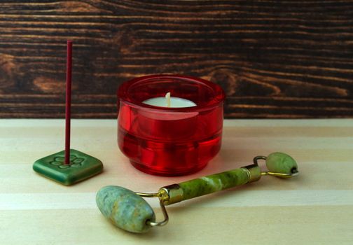 A jade roller, a candle and an incense stick, on a wooden table.