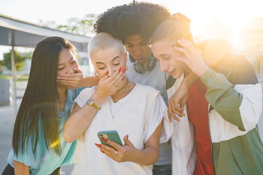 Cheerful group of friends looking smart phone surprised and excited outdoors. Smiling young people sharing with cell phones having fun together. High quality photo