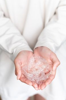 A woman's hand holds invisible aligners in the palms against the background of herself in a white sweater, close-up. No face, unrecognizable person.