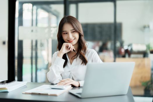 Portrait of a woman business owner showing a happy smiling face as he has successfully invested her business using computers and financial budget documents at work.