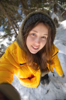 Young Caucasian beautiful woman smiling. Taking a selfie photo with a camera in winter, in a snowy forest. Girl outdoors. Walk in the park.