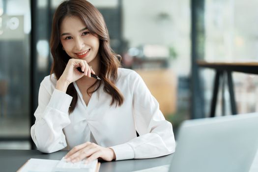 Portrait of a woman business owner showing a happy smiling face as he has successfully invested her business using computers and financial budget documents at work.