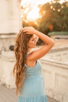 Woman sunset blue dress. Portrait of a woman with long hair and a blue dress against the backdrop of the setting sun and a white building. Lifestyle, walking around the city.