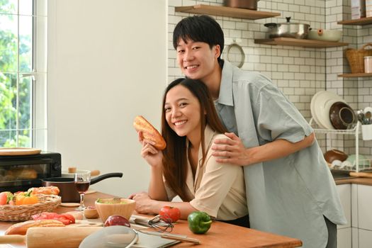 Romantic young couple is talking while cooking healthy food in kitchen, spending free weekend time together at home.