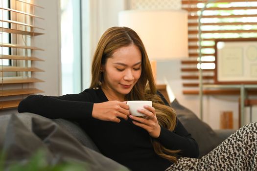 Relaxed woman in casual clothes enjoying her morning coffee on comfortable couch at home.